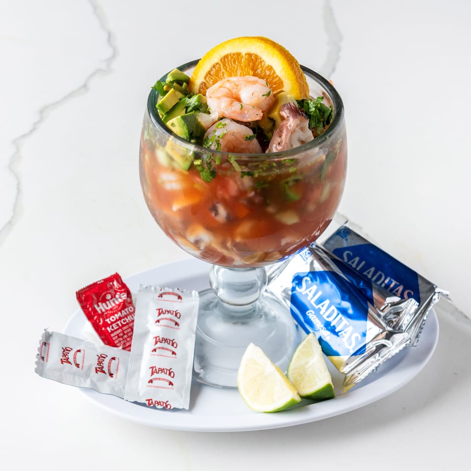 Shrimp cocktail in a goblet with avocado, orange, lime, ketchup, hot sauce, and crackers.
