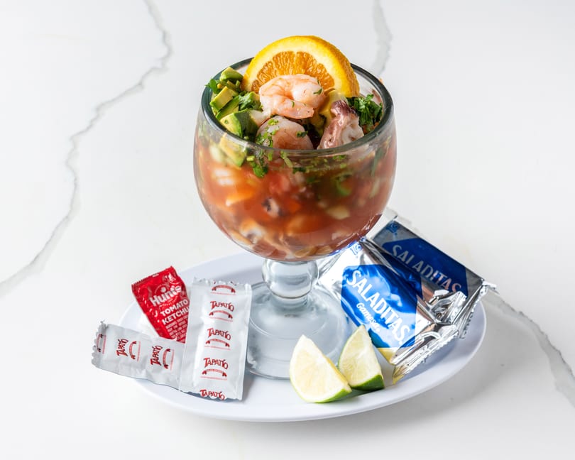 Shrimp cocktail in a goblet with avocado, orange, lime, ketchup, hot sauce, and crackers.