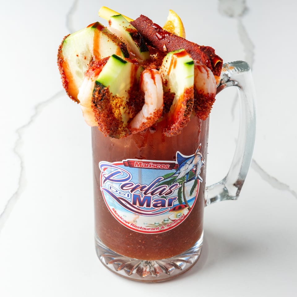 A michelada with shrimp, cucumber, and chili powder in a branded glass mug.