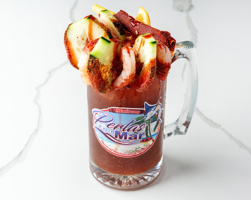 A michelada with shrimp, cucumber, and chili powder in a branded glass mug.