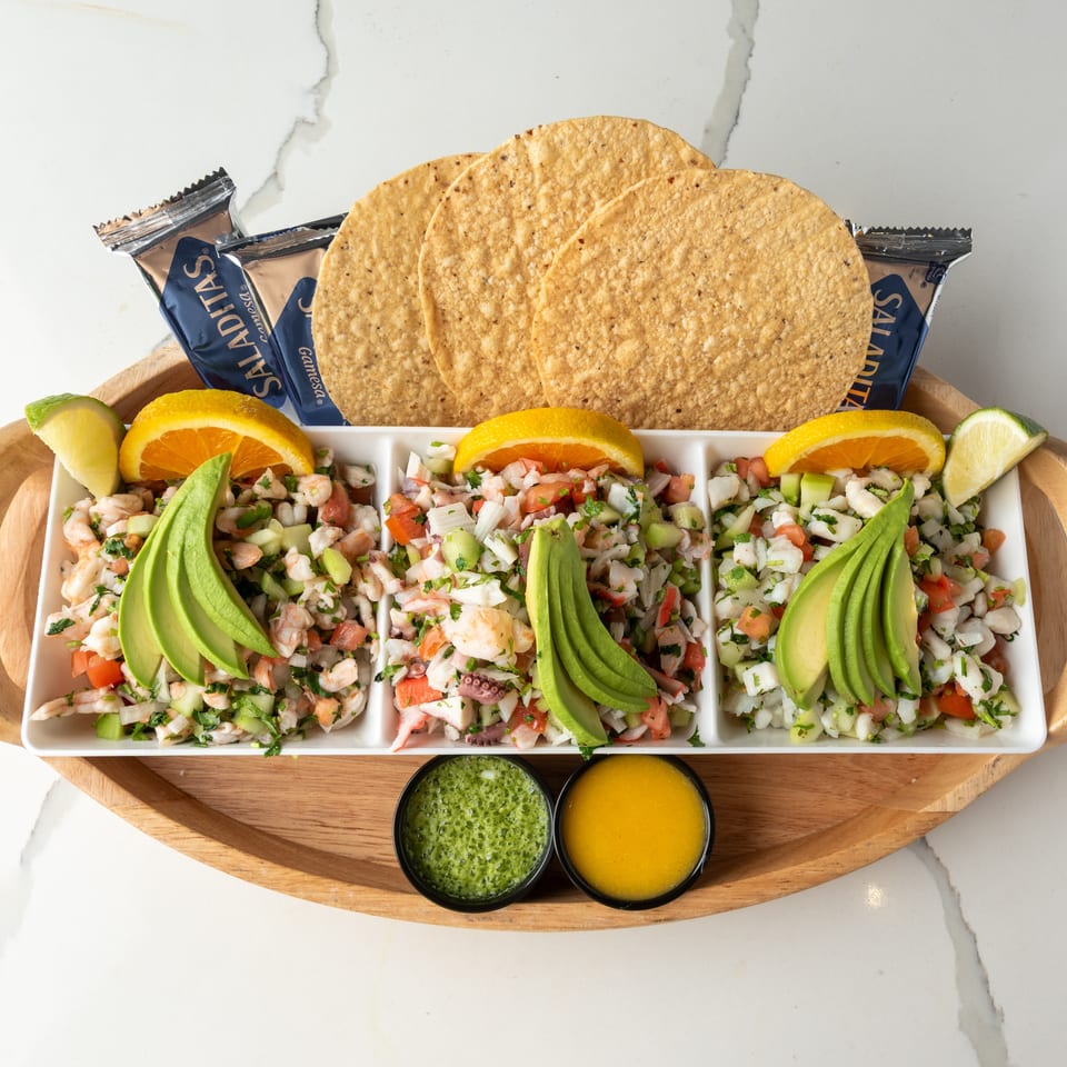 Three types of ceviche with avocado, orange, lime, tostadas, and sauces on a wooden tray.