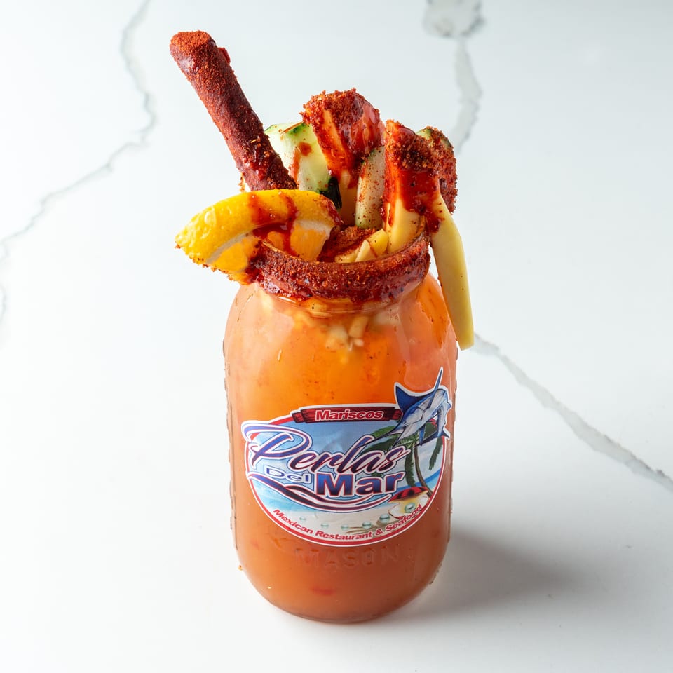 A Perlas Del Mar Michelada, garnished with cucumber, mango, lemon, and a tamarind candy straw.