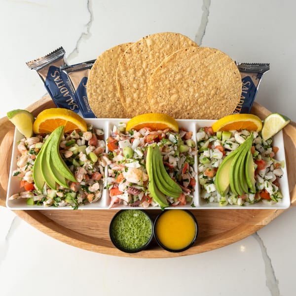 Three types of ceviche with avocado, orange, and lime, served with tostadas and sauces.